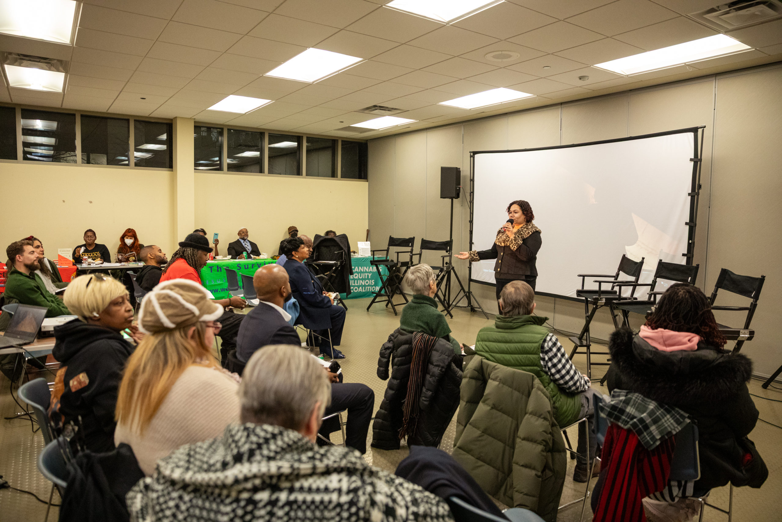 NPTP Employee Jazmine Salas stands at the front of a room holding a microphone, and presenting to a crowd of people.
